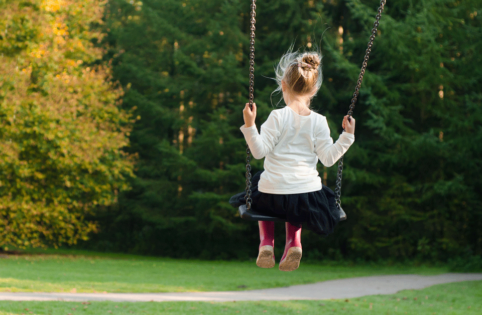 Young girl swinging in a green park