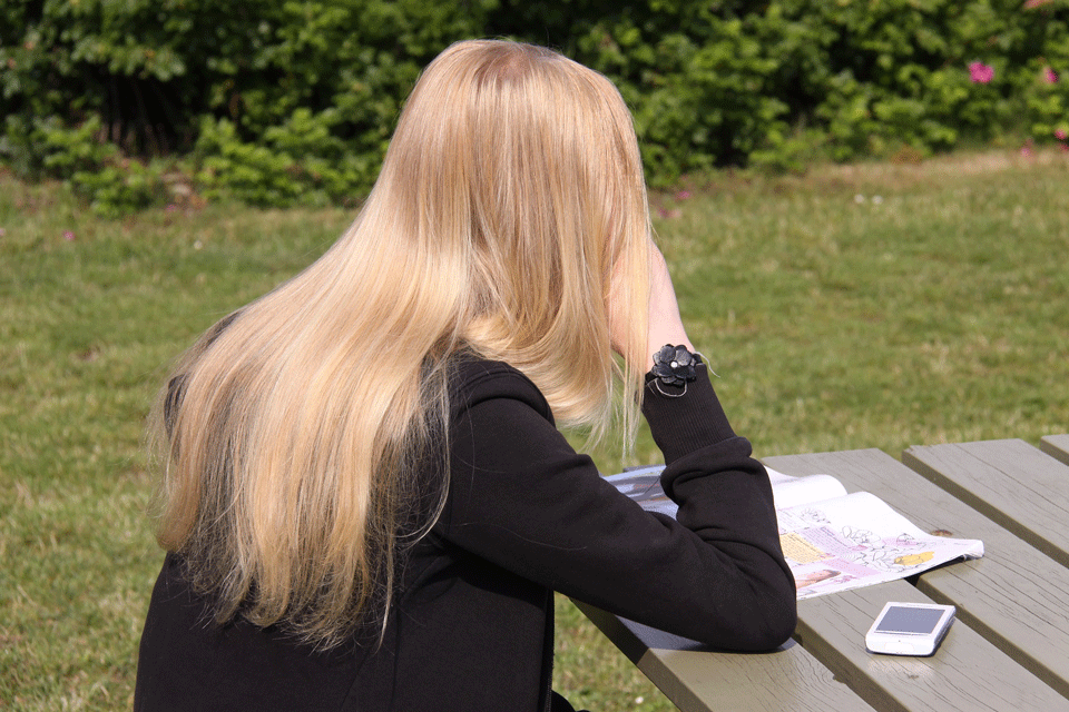 Teenage girl with blonde long hair sitting with back to photographer at a picnic table