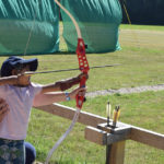 child being guided by Rebecca in the archery