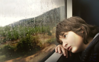 Bored child looking out of a raindrop covered window