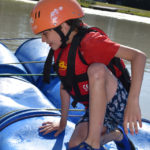 child kneeling on a barrel while raft being built