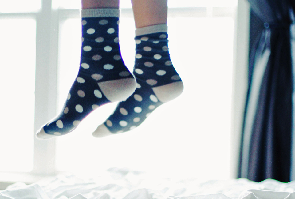 Child's feet in socks bouncing on the bed by Rafael Lodos