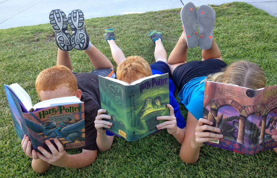 three children lying on the grass reading Harry Potter books