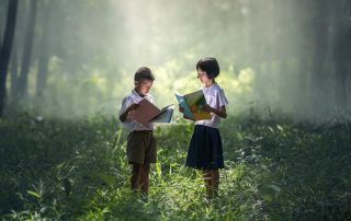 Two children standing in a forest reading books