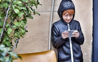 statue of a child in a hoodie looking at a mobile