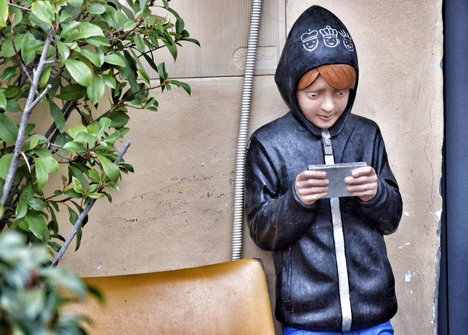 statue of a child in a hoodie looking at a mobile