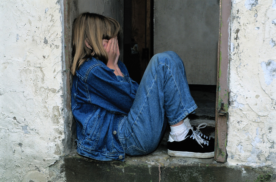 Child sitting in a doorway with hands over her face