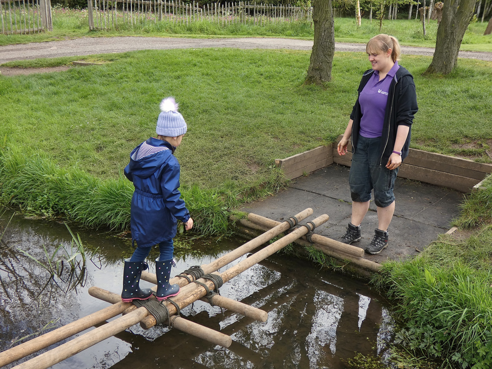 Girl crossing a stream on a pole bridge she helped build at the PPUK Be Curious Weekend 2019