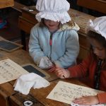Two girls dressed in victorian mobcaps practising copperplate handwriting at the PPUK Be Curious Weekend 2019