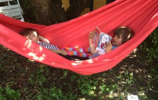 Noah, aged 6, reading Shakespeare to Rosa, aged 2 in a red hammock