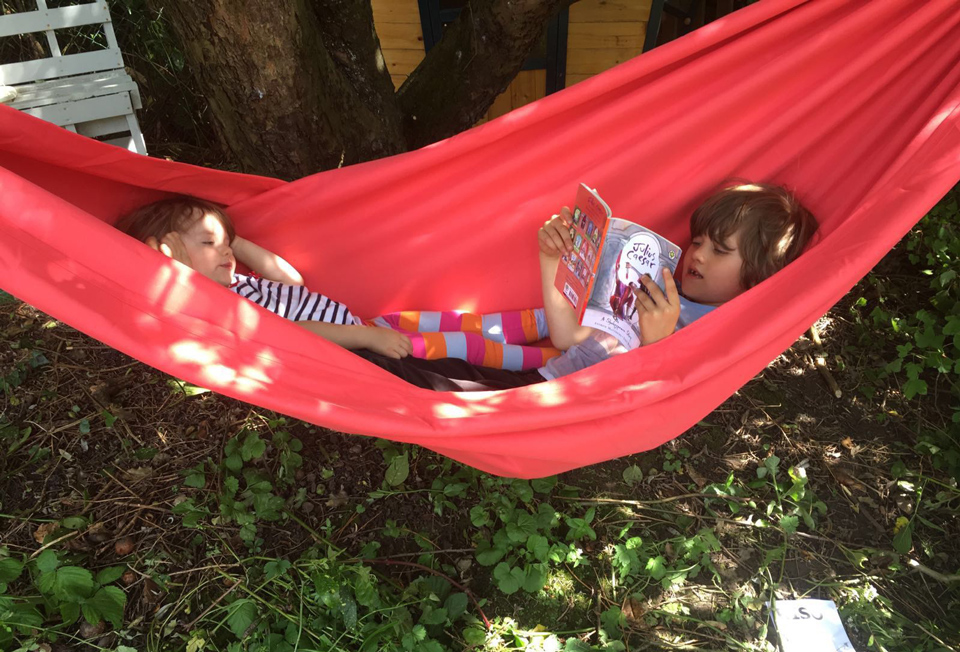 Noah, aged 6, reading Shakespeare to Rosa, aged 2 in a red hammock