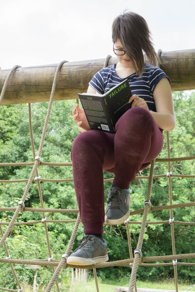 girl reading a book at the top of an obstacle course net