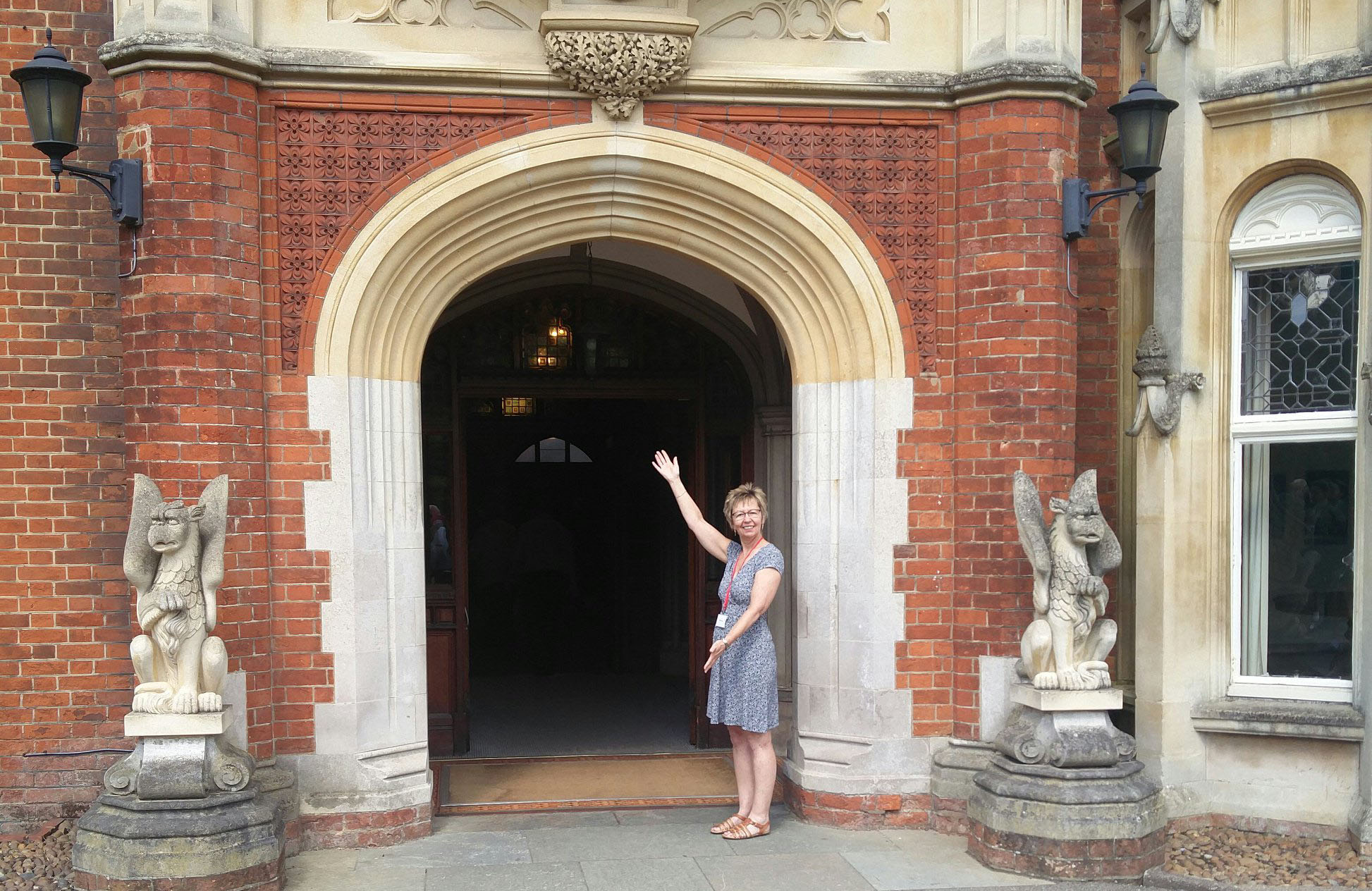 Julie Taplin standing with arms in a welcoming stance outside the entrance door to The Mansion, Bletchley Park, July 2019