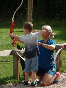 young boy being helped to fire an arrow