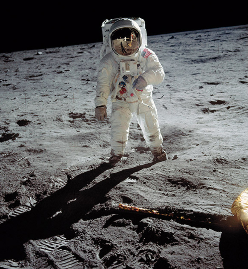 Buzz Aldrin on the surface of the moon photographed by Neil Armstrong who is reflected in the helmet