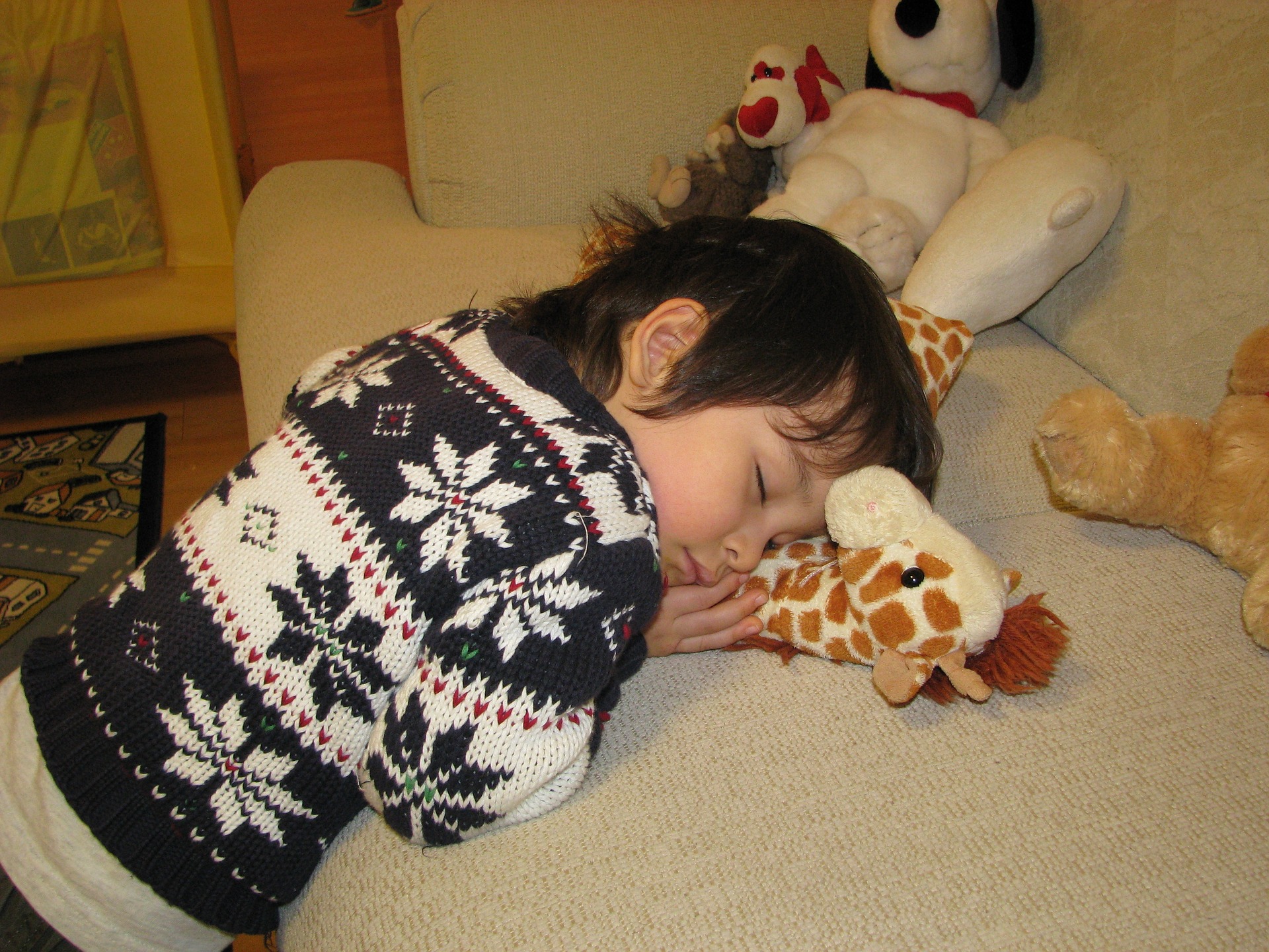 Child asleep on the sofa hugging a soft toy giraffe