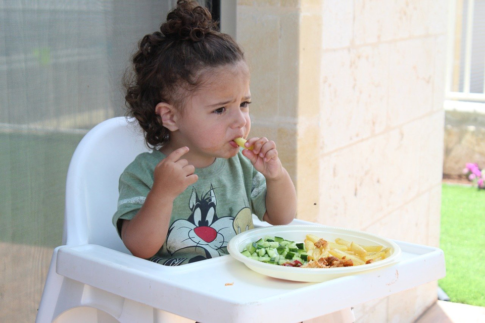 Child in a high chair not sure whether she is happy eating or not