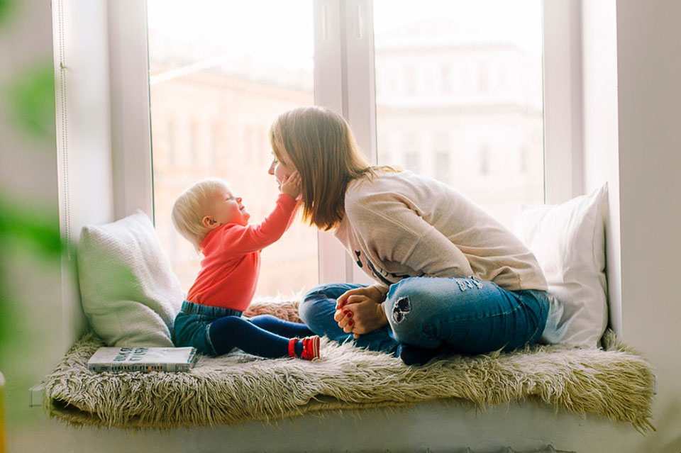 young child touching a woman's face while sitting in a window seat