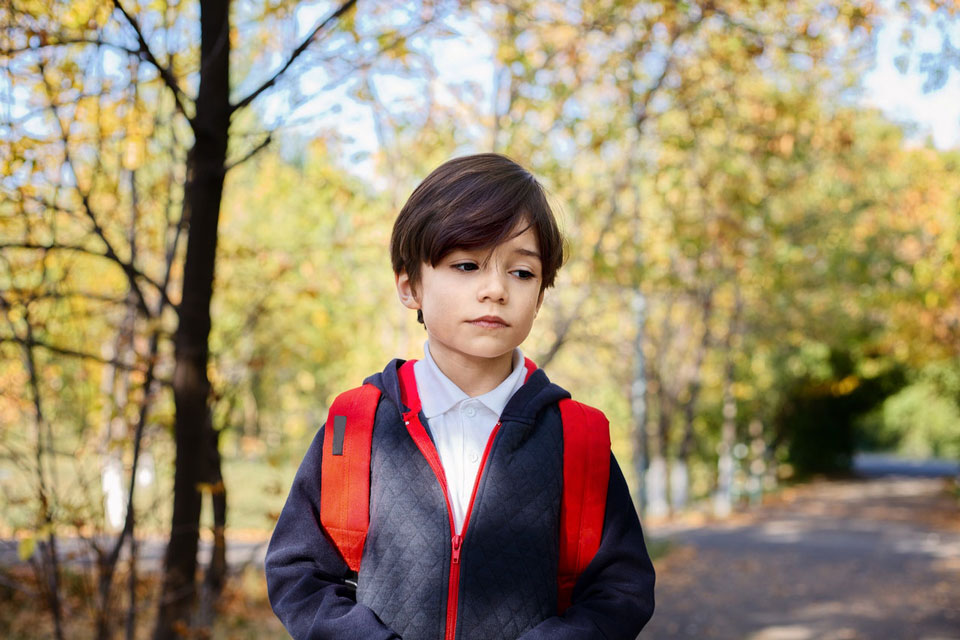 Sad schoolboy standing in a park