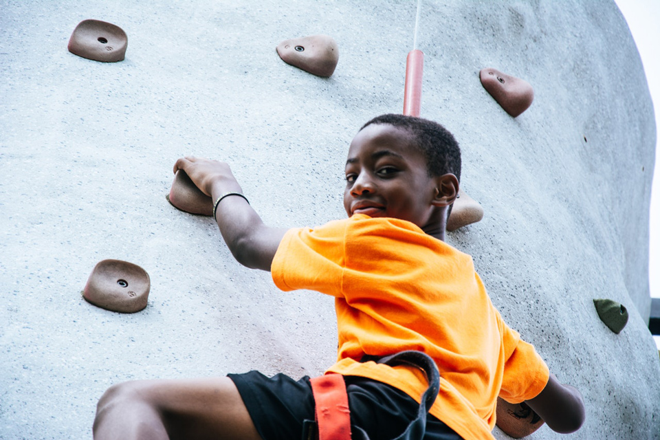 Boy half way up a climbing wall looking back at the camera and smiling