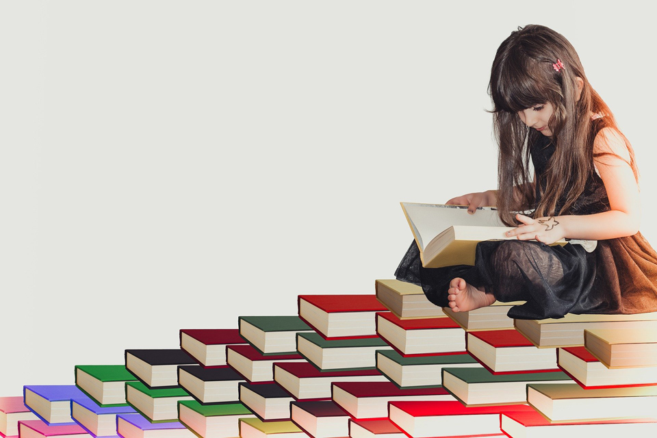 Photo of a girl reading perched on a stack of books