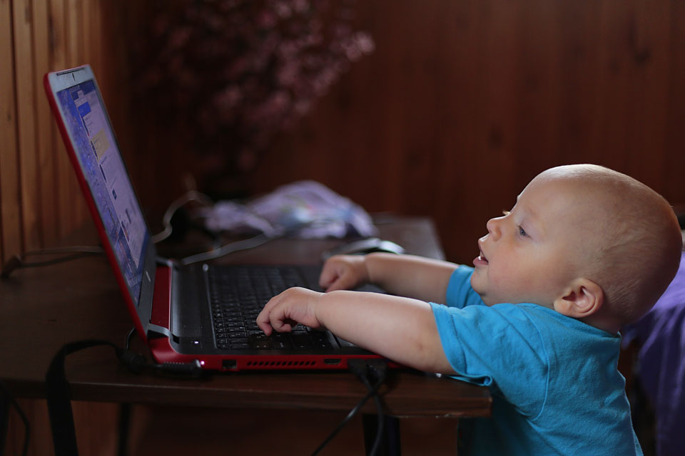 toddler reaching up to a table to play on a laptop
