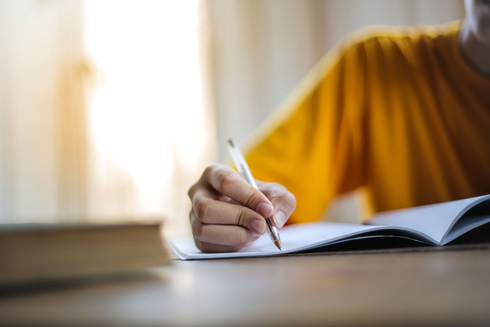 Hand of an adult holding a pen writing in a booklet