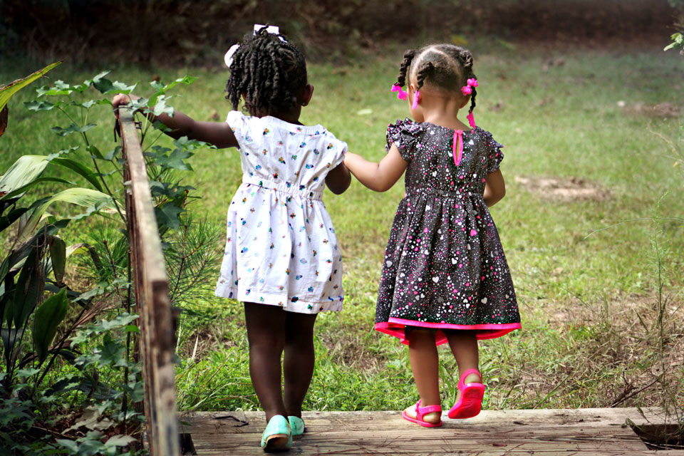 Two very young girls walking hand in hand over a bridge
