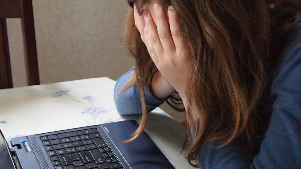 child in front of a laptop with head in hands crying