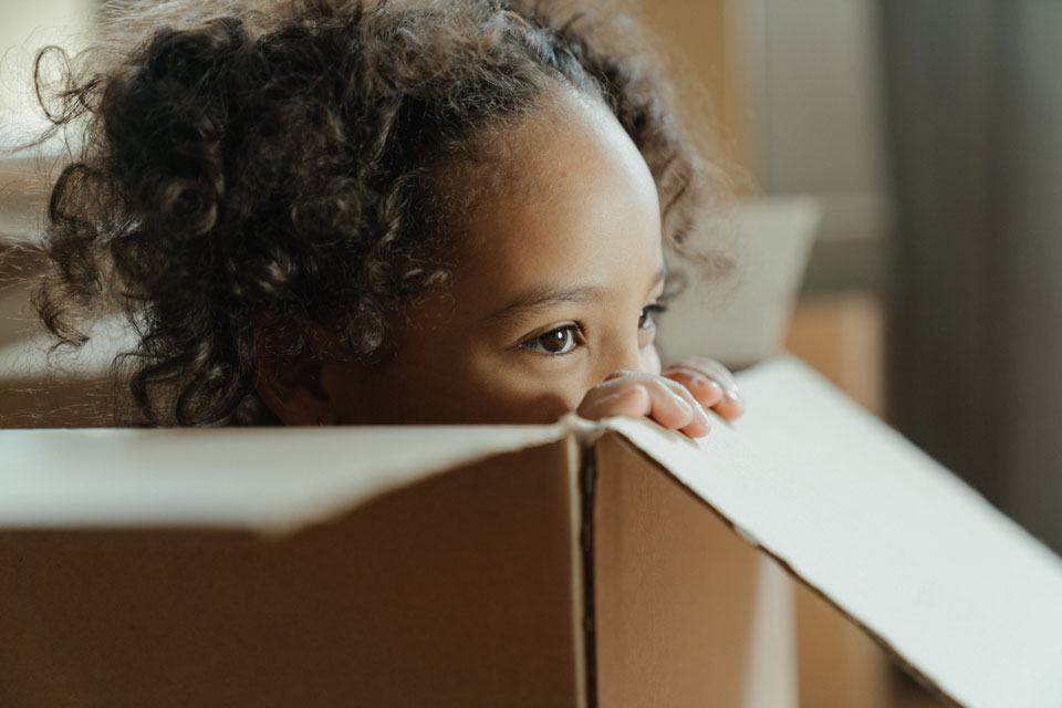 Young child looking over the edge of a cardboard box she is sitting in