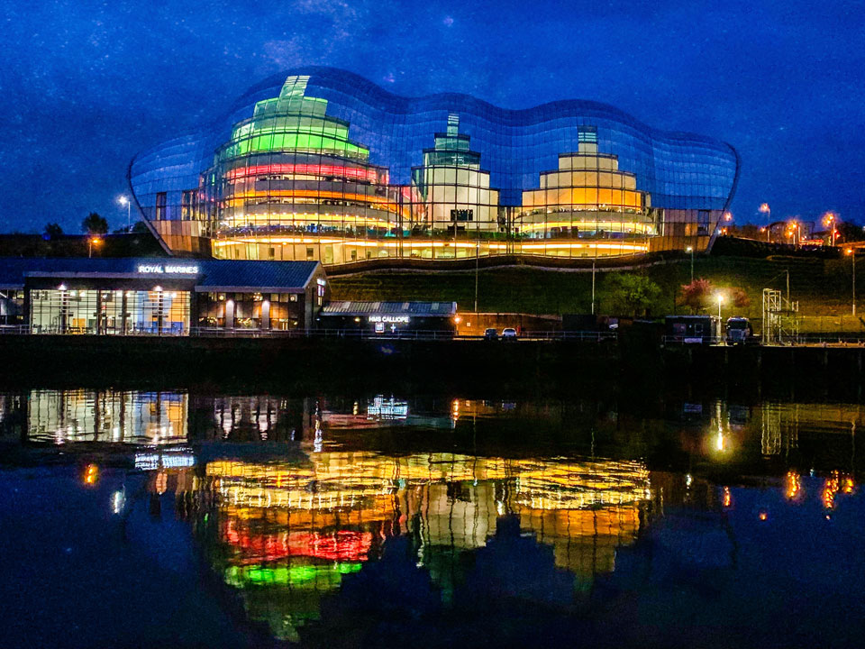 Nighttime shot. Lights of buildings, reflected on the Sage Building, Gateshead and the river Tyne below