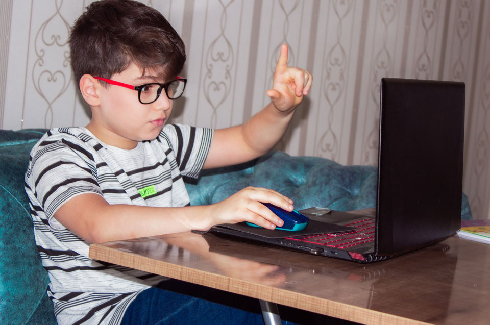 boy sitting in front of a laptop with hand raised
