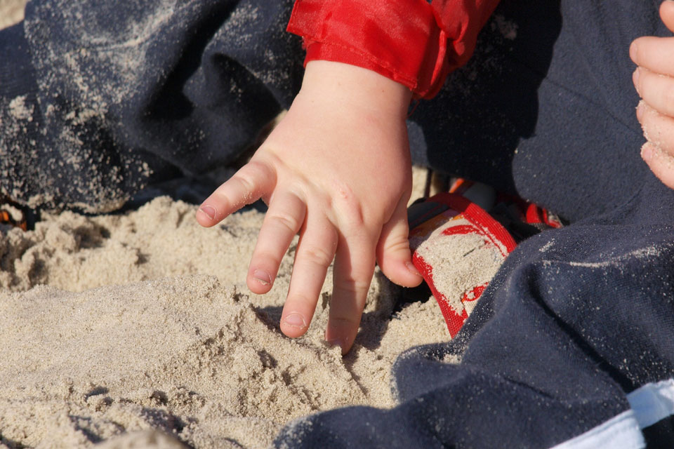 child tentatively touching sand