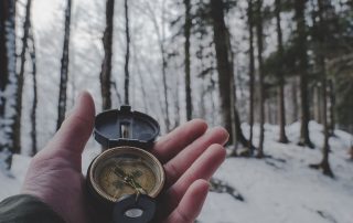 Hand holding a compass in a snowy woodland scene