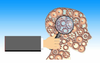 Hand holding a magnifying glass towards a stylistic cog representation of the brain and head