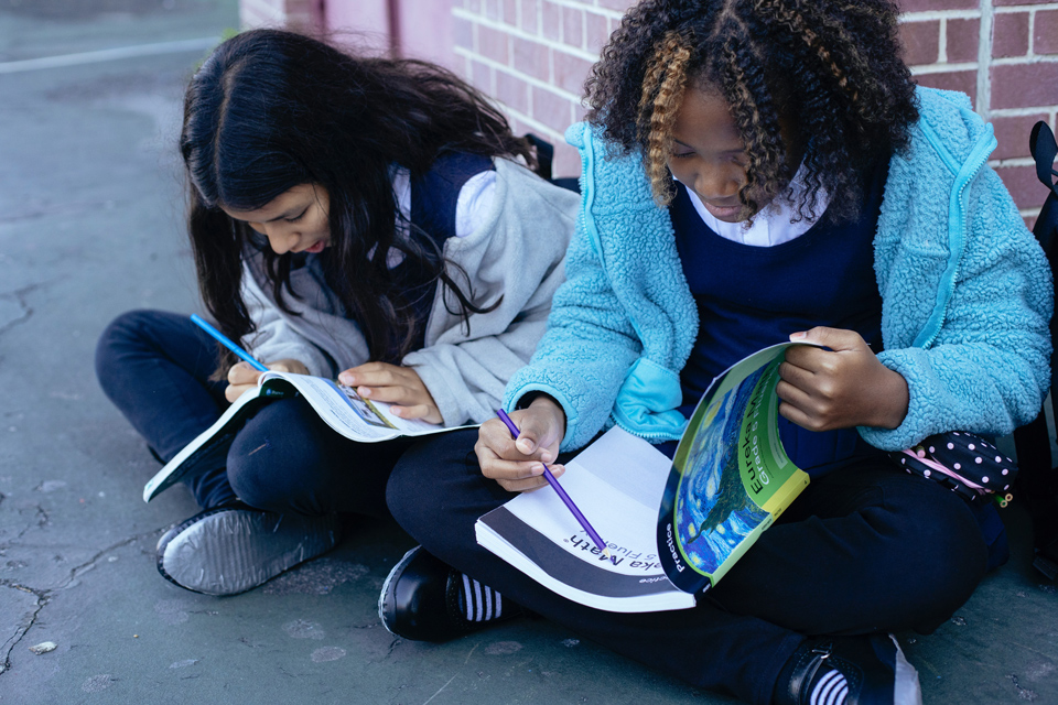 two teenager sitting on the ground going through workbooks