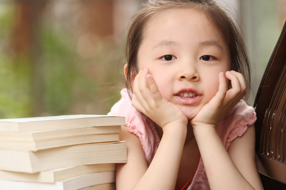 Young child leaning on her hands with a pile of books beside her