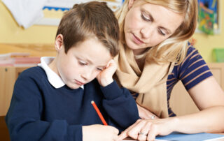 female teacher helping male primary school child with handwriting problem