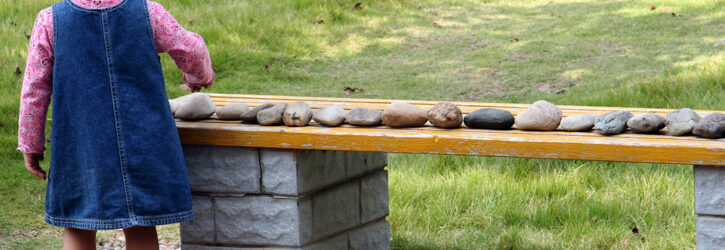 young toddler lining up stones on a bench