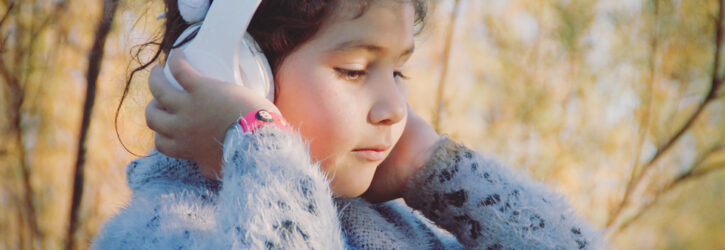Young girl holding headphones to her ears in a woodland setting