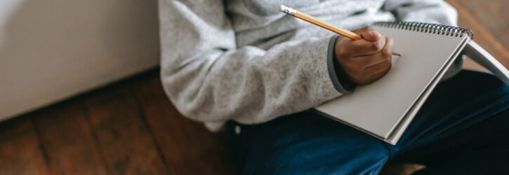 boy sitting on the ground with notepad and pencil