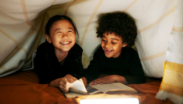Two children lying in a bed tent reading