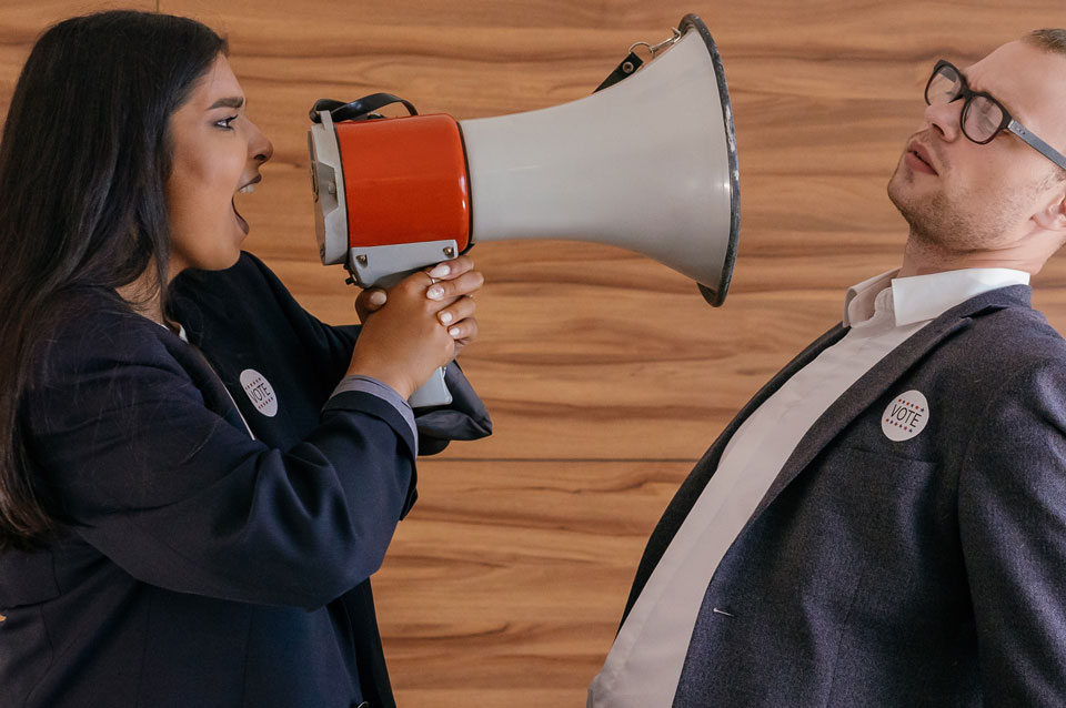 Woman with megaphone shouting to man leaning back directly in front of him