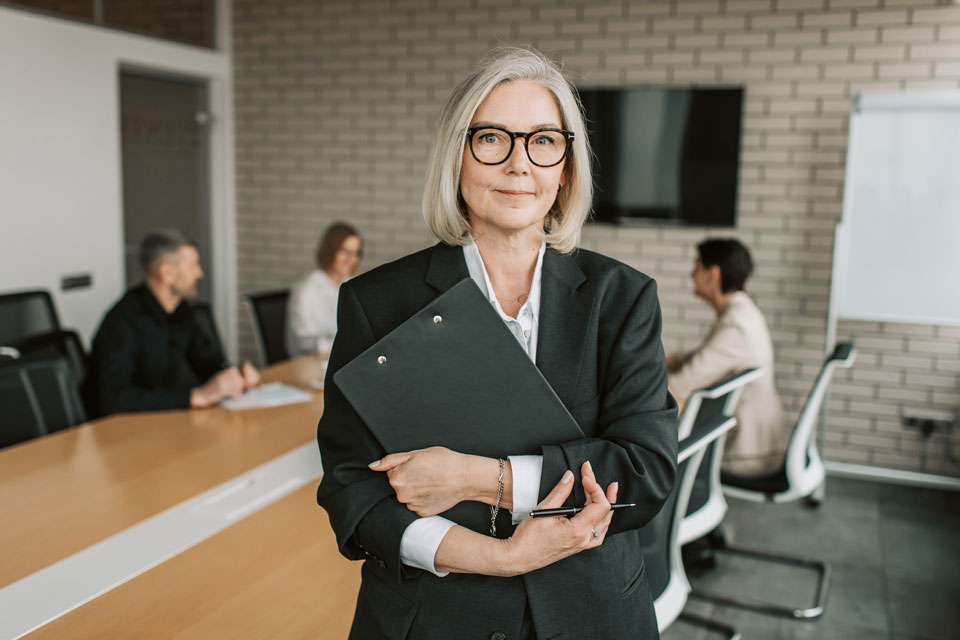 teacher standing holding a clipboard in front of a group of people sitting at a table