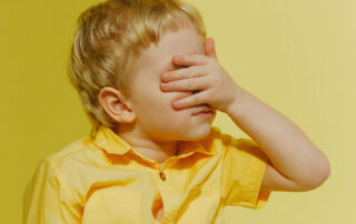 Child in yellow top in yellow room with hands over eyes