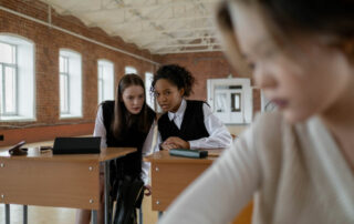 girl sitting isolated with a couple of girls huddled in classroom gossiping about her