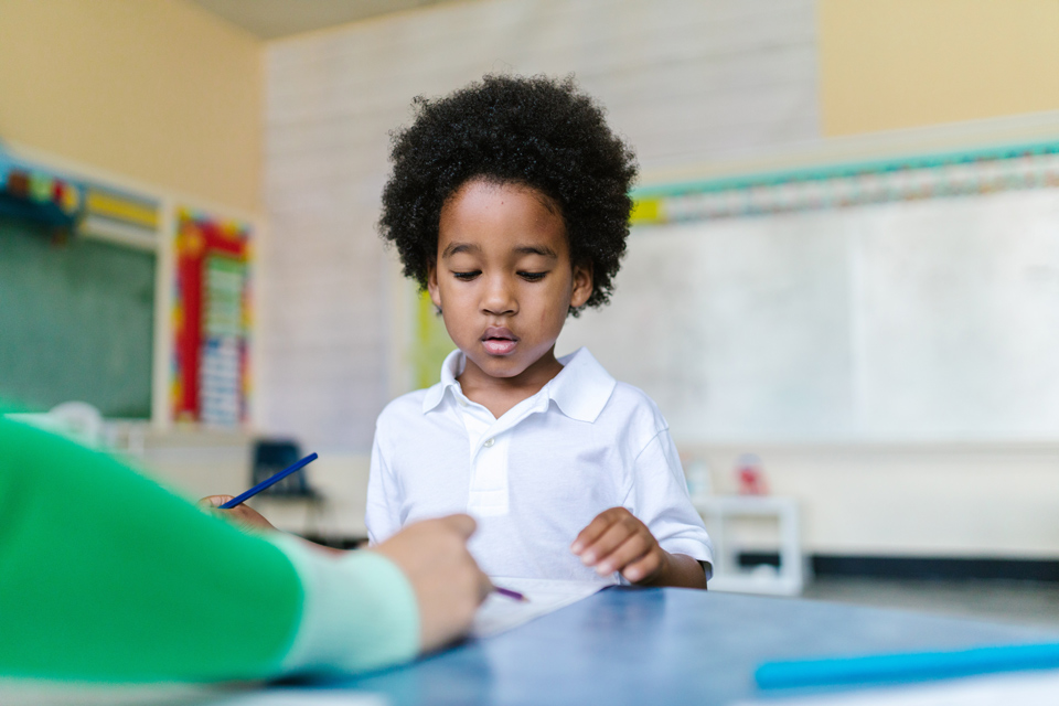 young child looking at something on desk being pointed out by teacher