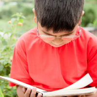 young boy sitting reading a book outdoors