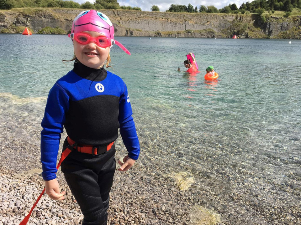 Young girl in wet suit standing next to open water swimming quarry