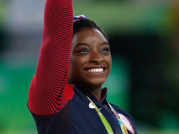 Simone Biles receiving her all-around gold medal at the Brazil 2016 Olympics. By Agência Brasil Fotografias - Crop of File:Simone Biles at the 2016 Olympics all-around gold medal podium (28262782114).jpg, CC BY 2.0, https://commons.wikimedia.org/w/index.php?curid=73989999